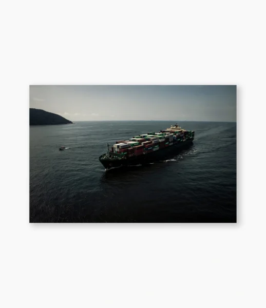 Pequena embarcação acompanhando navio cargueiro, montanhas ao fundo – fotografia de André Nunez